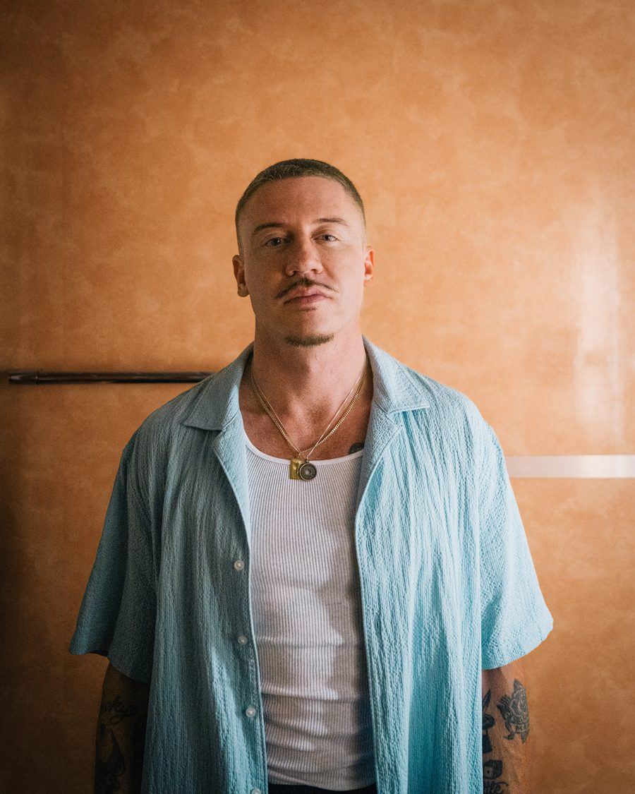 Portrait of Macklemore in a light blue shirt against an orange wall