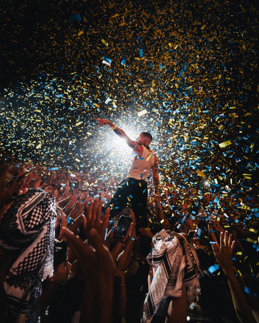Macklemore pointing out over the crowd under a storm of blue and yellow confetti