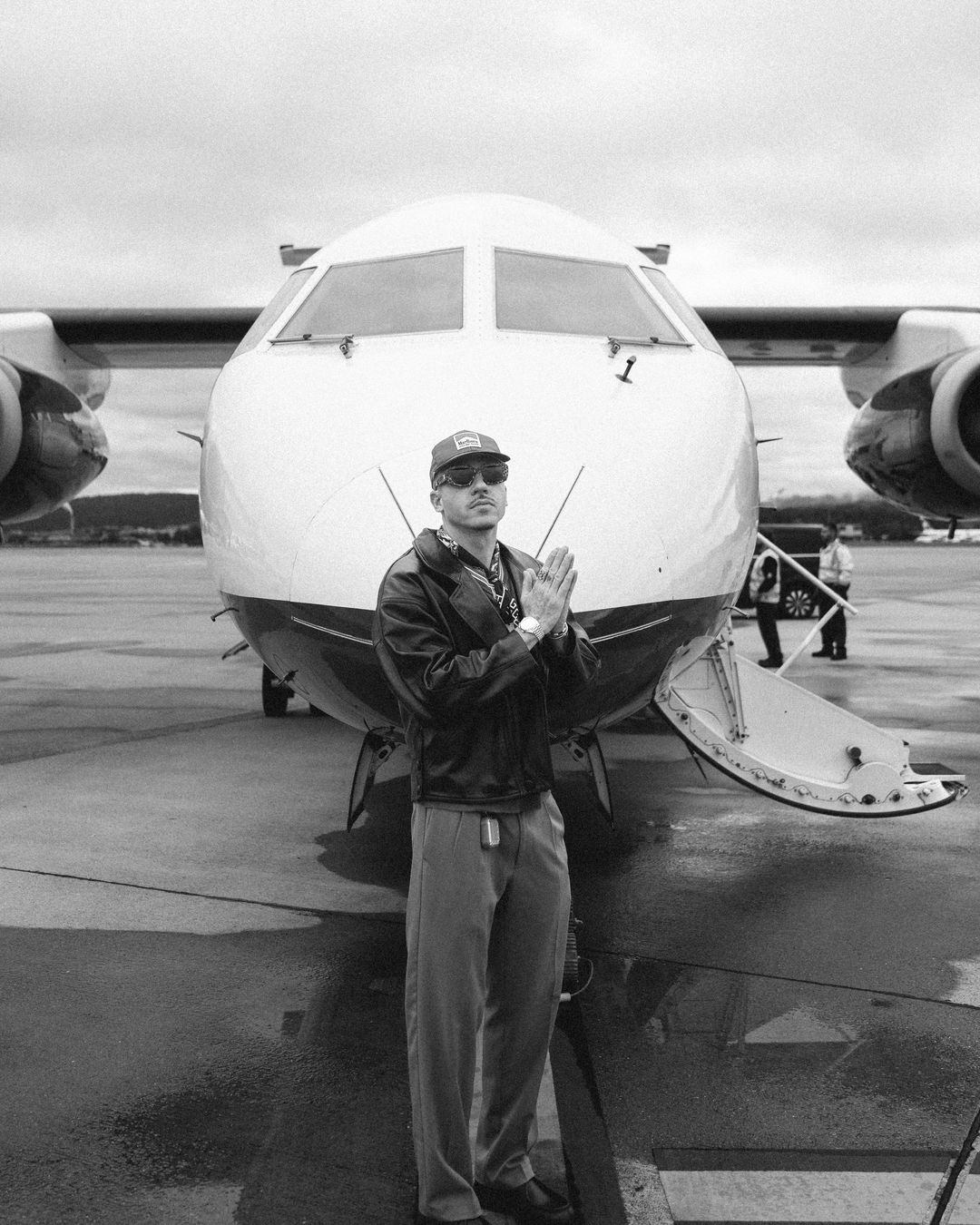 Macklemore on the tarmac in front of a private jet, hands pressed together
