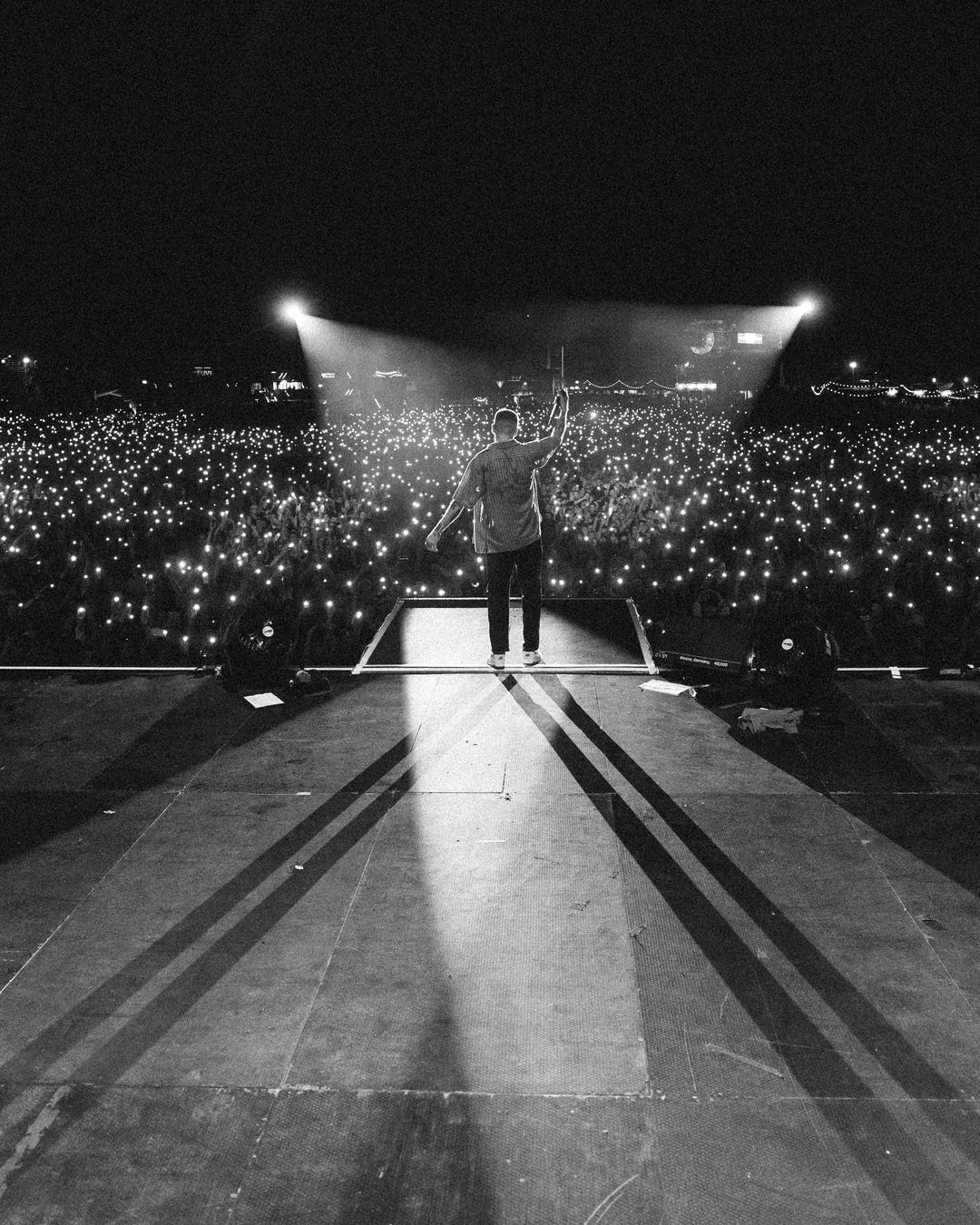 Macklemore alone at the front of the stage facing a sea of phone lights