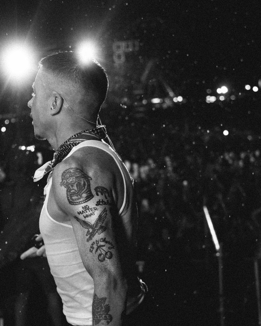 Macklemore on stage in a white tank top, tattoos lit by stage lights
