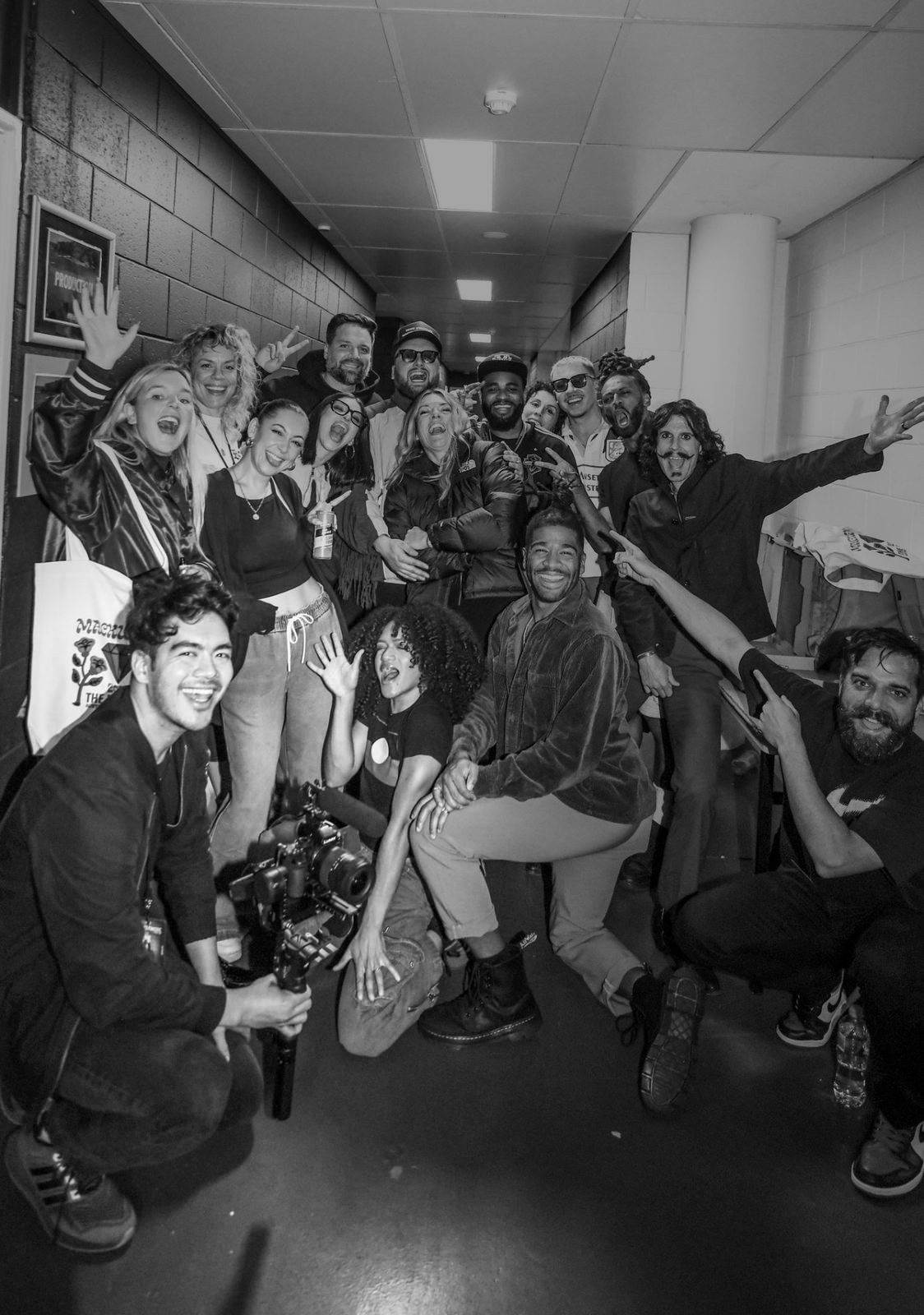 Black and white photo of the BEN Tour crew backstage, with Charles crouched at front left holding a camera rig